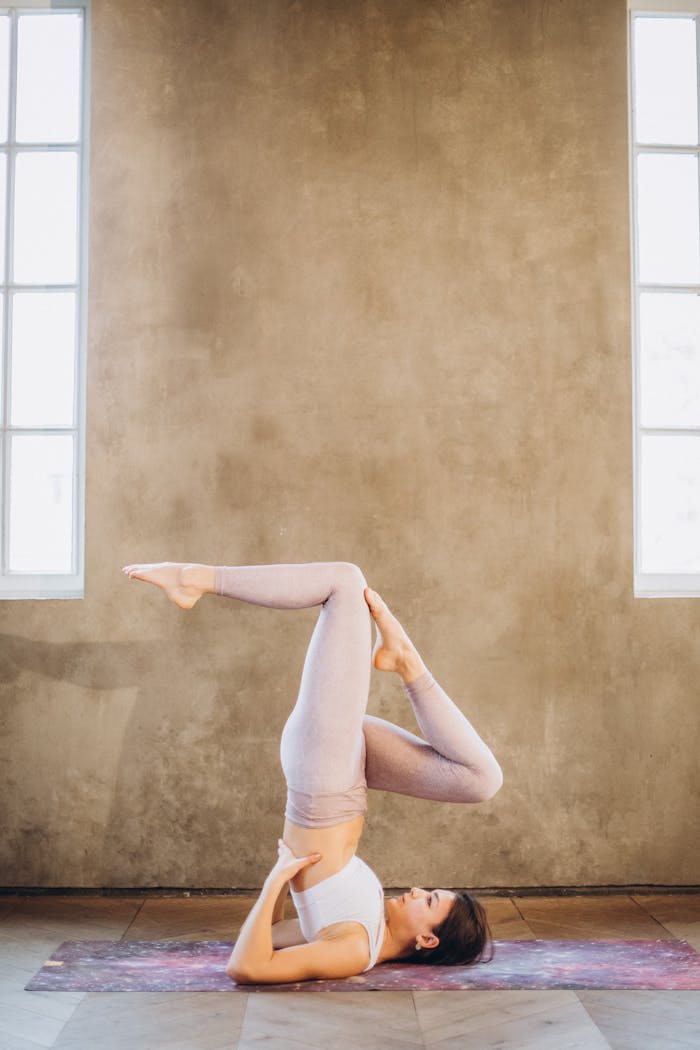 A woman performing a yoga shoulderstand pose indoors, focusing on flexibility and relaxation.